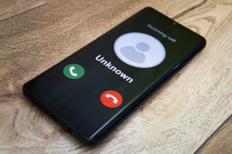 A smartphone on a wooden table displaying an incoming call from an unknown phone number.