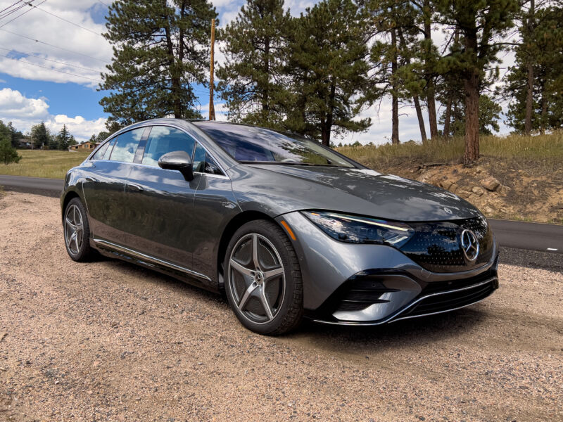 A dark grey Mercedes EQE sedan parked in front of some trees