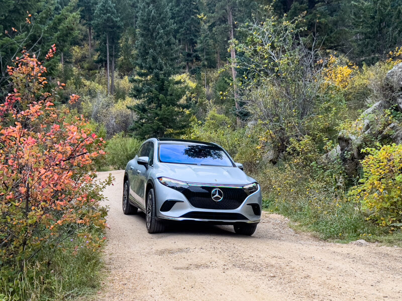 A silver Mercedes EQS SUV on a dirt road between some colorful bushes and trees