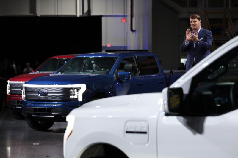 A man in a suit stands next to three trucks