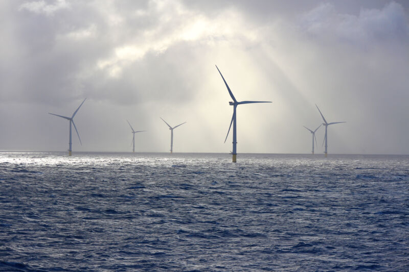 Image of offshore wind turbines lit by sunlight filtered through clouds.