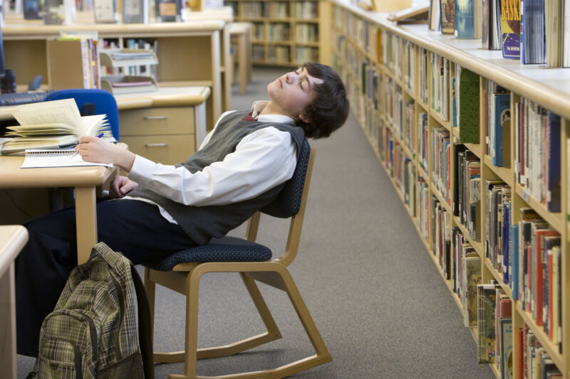 Image of a teen in a library, slumped over in his chair.l