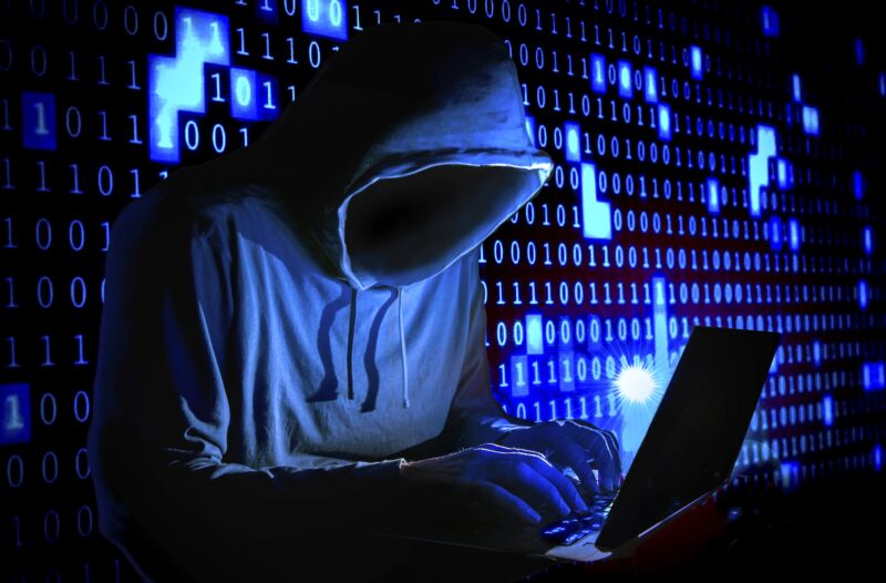 Illustration of a hooded figure in dark room typing on a laptop. In the background, the wall is covered in ones and zeroes.
