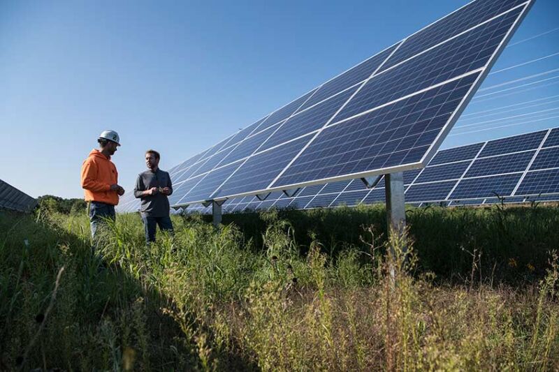 Imagen de dos personas de pie frente a paneles solares.