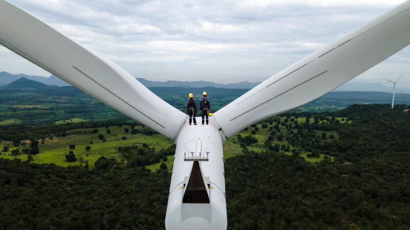 Two people standing on the nacelle of a wind turbine.