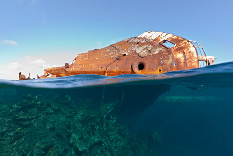 Image of a rusty ship hull tilted over on its side in the water.