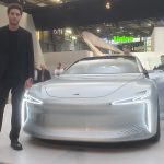 A man stands next to a futuristic silver sedan