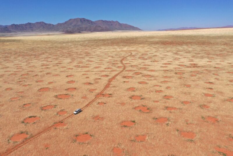 Dronebeeld van een auto die door het NamibRand Nature Reserve rijdt, een gebied van de Fairy Circle in Namibië.