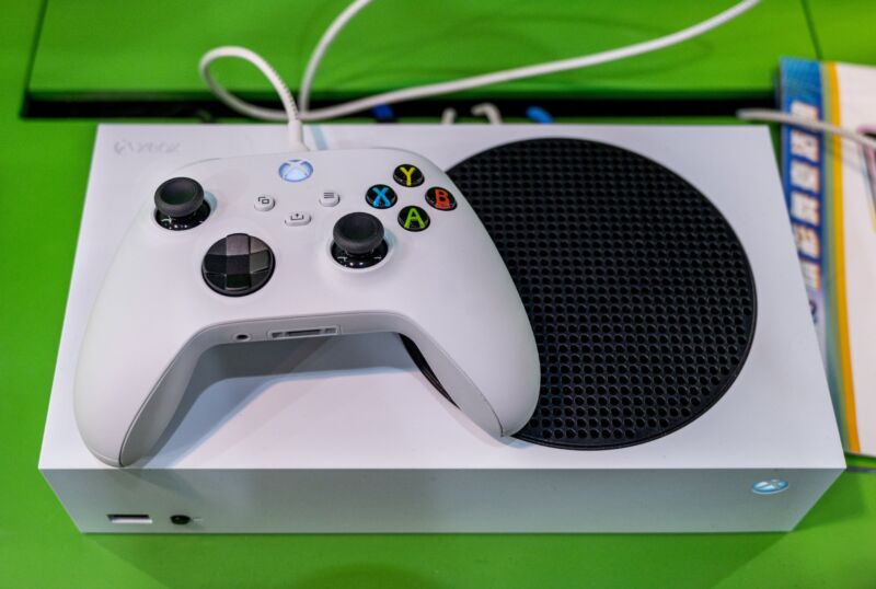 An Xbox controller sitting connected  apical  of an Xbox Series S console.