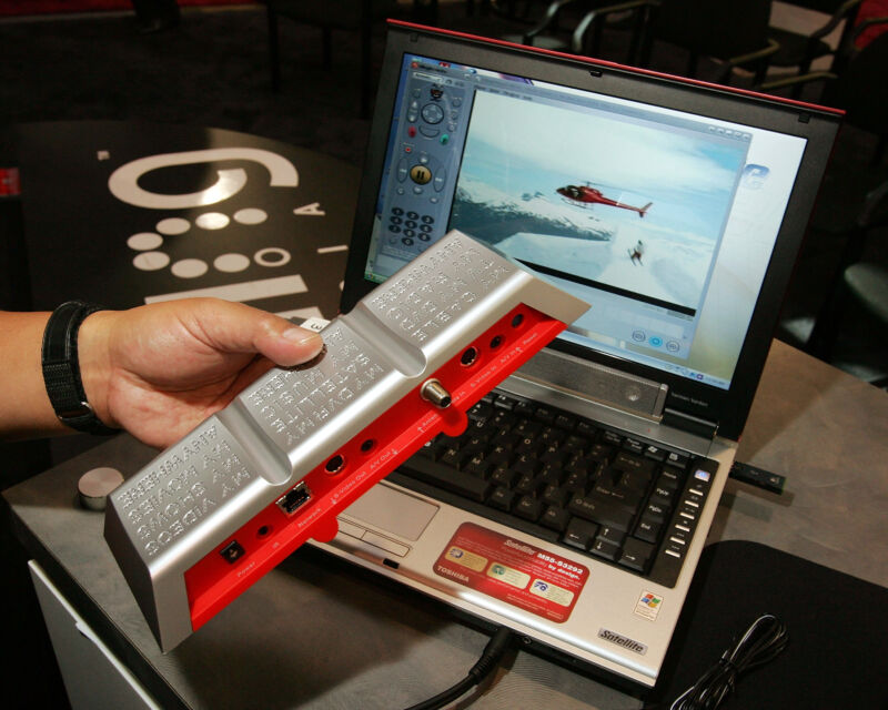 The original Slingbox, on display at the 2006 Consumer Electronics Show. Key indicators of this being a long time ago include the Toshiba Satellite laptop used for the demonstration (and the giant glossy UI buttons).