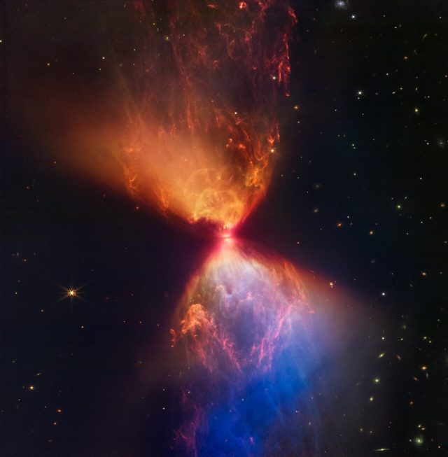 Material ejected from the star has cleared out cavities above and below it, whose boundaries glow orange and blue in this infrared view. 