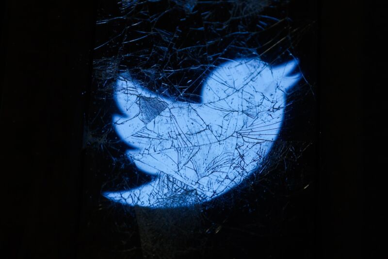 The Twitter logo displayed on a cracked phone screen is seen through broken glass