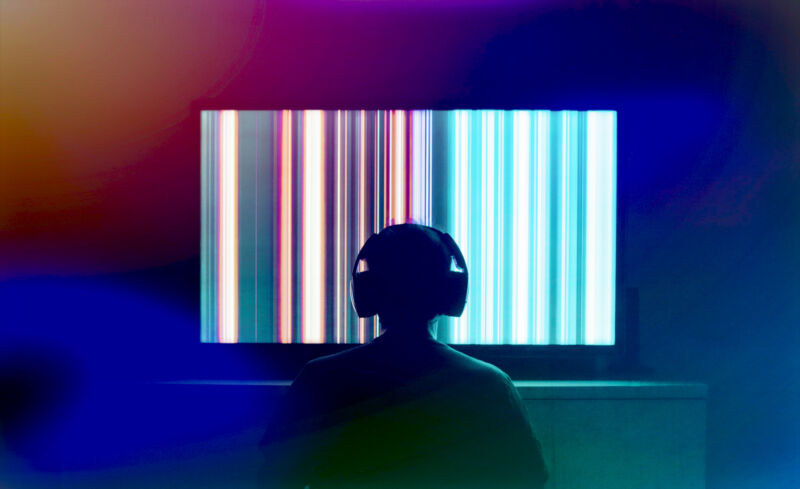 Silhouetted person with headphones watching large OLED screen