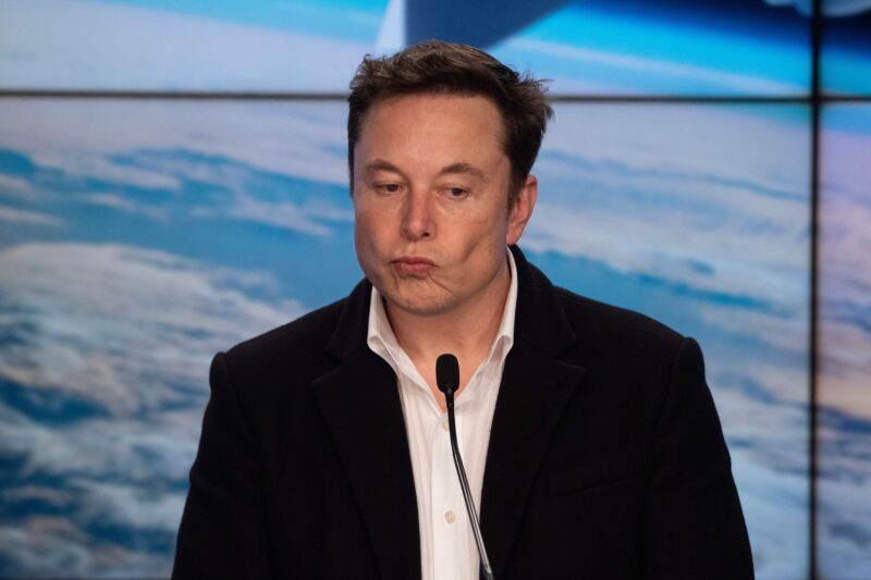 Elon Musk standing in front of a microphone during a press conference