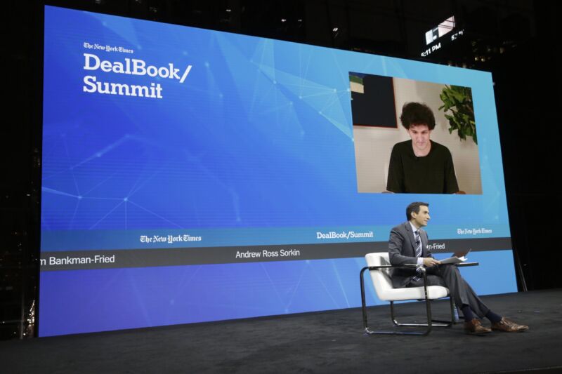 Journalist Andrew Ross Sorkin sitting on stage at a conference while interviewing Sam Bankman-Fried, who appeared remotely and was seen on a giant video screen.