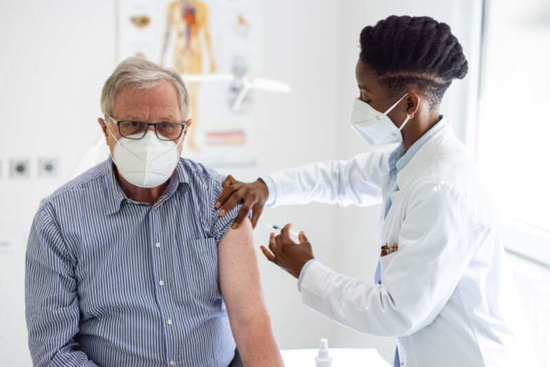 A medical professional administers an injection to the arm of a seated person.