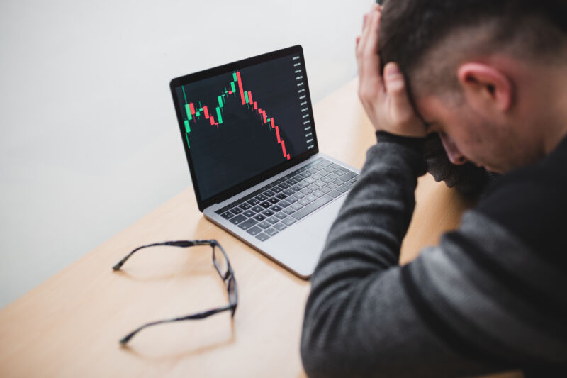 Hombre sosteniendo la cabeza en las manos frente a la computadora portátil que muestra precios de caída