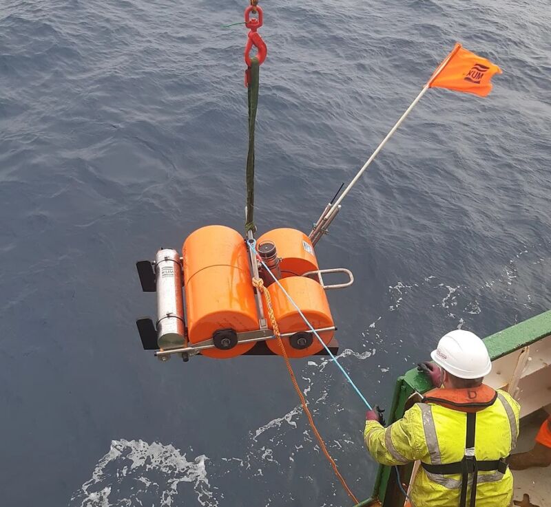 Imagen de una persona con un casco que guía un gran dispositivo naranja mientras desciende al océano.