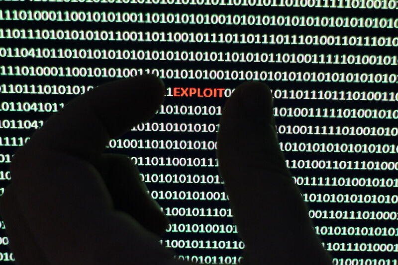 Photograph depicts a security scanner extracting virus from a string of binary code. Hand with the word &quot;exploit&quot;