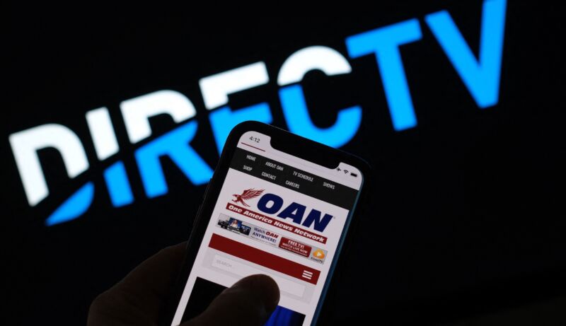 One America News website displayed on a phone screen. A DirecTV logo is seen in the background.
