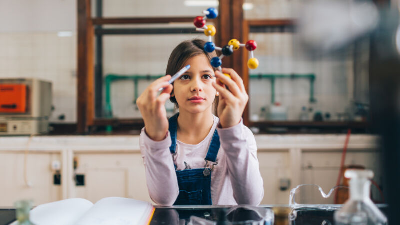 Image of a girl holding up a ball-and-stick model of a molecule in a classroom.