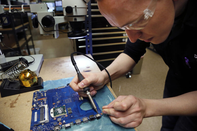 Repair shop technician solders on laptop-size circuit board