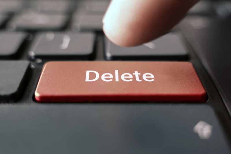 A person's finger hovering over a keyboard's delete key.