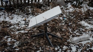 A Starlink antenna sitting on the ground, with patches of snow around it.