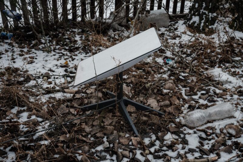 A Starlink antenna sitting on the ground, with patches of snow around it.