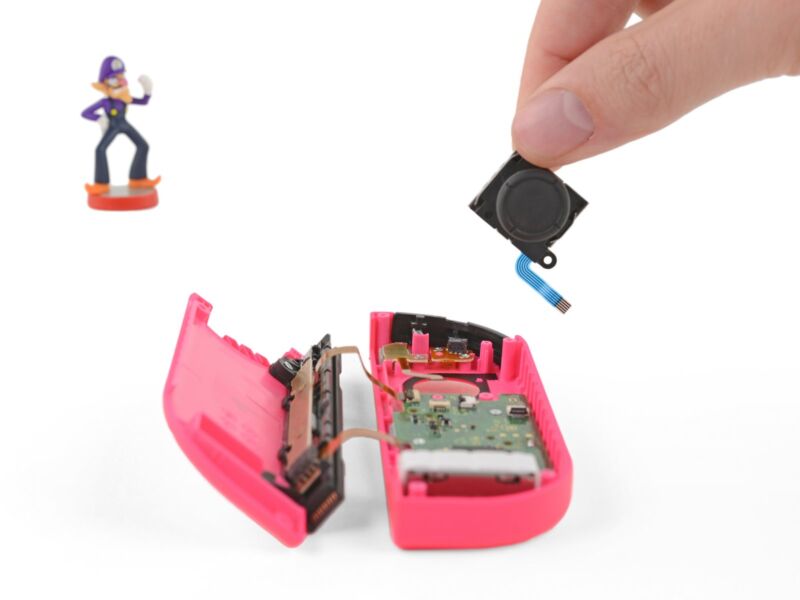 Waluigi figurine shaking fist at a joystick removed from a Joy-Con