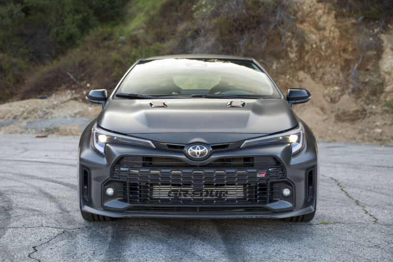 A dark grey Toyota GR Corolla seen head-on. It has a very large front grille and many air intakes and flared arches