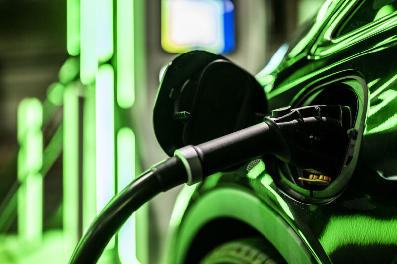 Close-up on an electric car charger plugged into car on public parking with electric charging stations.