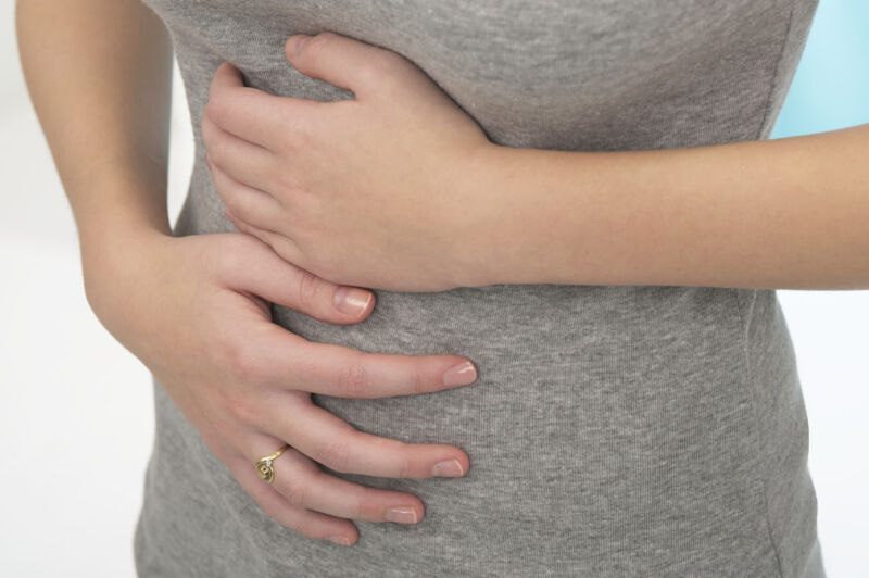 A woman experiencing abdominal pain by covering both hands over her stomach.