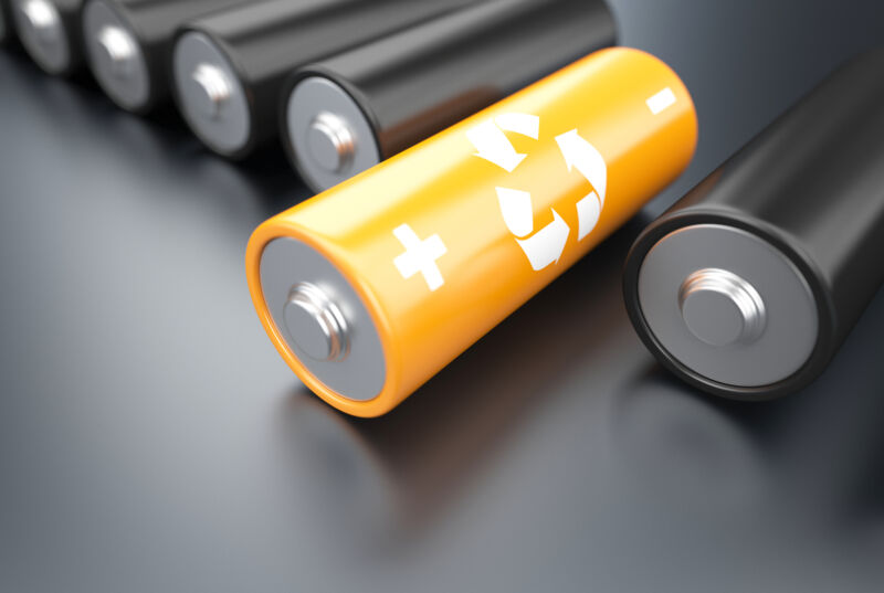Battery recycling concept. Orange eco battery with black batteries on dark background