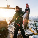 A man on a boat holding a large fish caught on a hook.