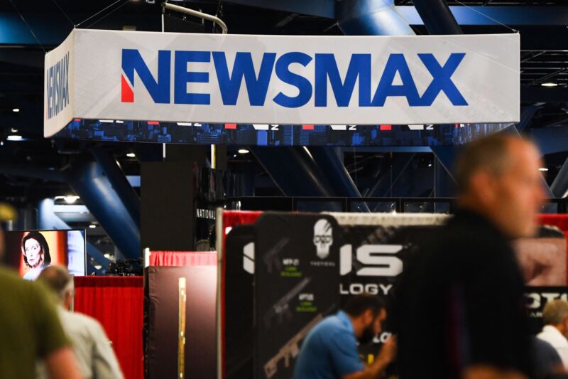 A large Newsmax logo on a booth on a conference floor.