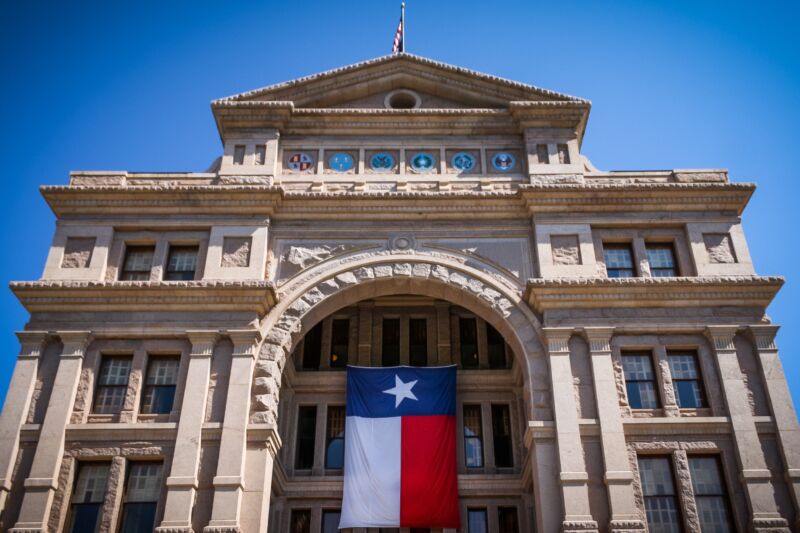The Texas state flag hanging on the outside of the state Capitol building during daytime.
