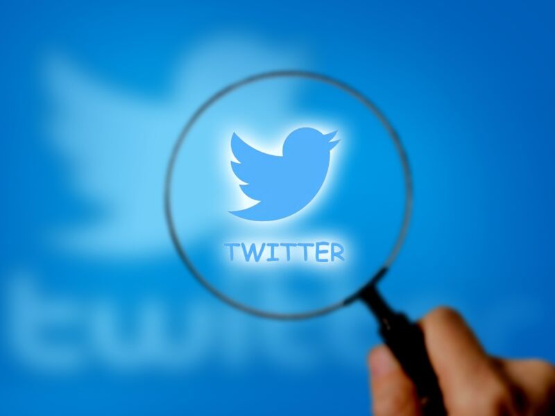 Illustration of a person's hand holding a magnifying glass over the Twitter logo.