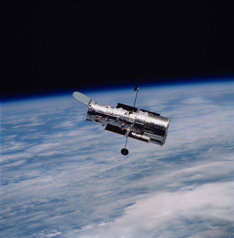 Image of the cylindrical Hubble space telescope in orbit above a cloudy Earth.