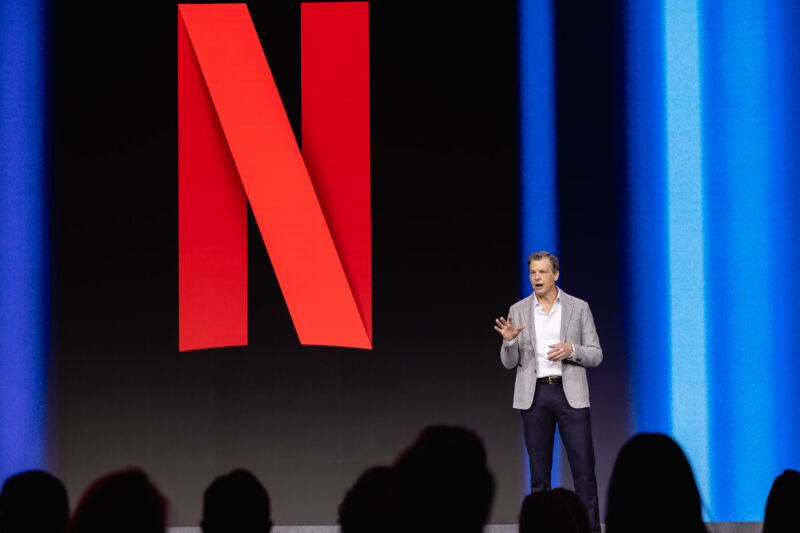 Netflix Co-CEO Greg Peters speaks on a stage with a Netflix logo in the backdrop.