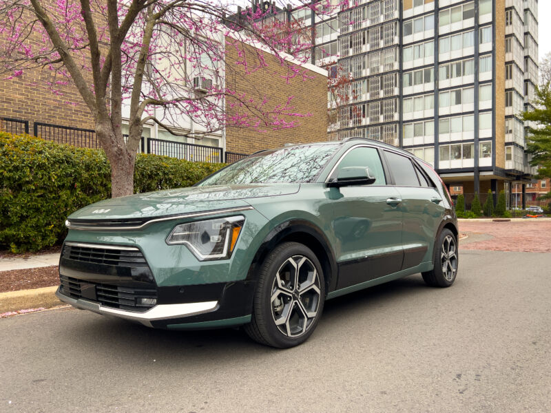 A green Kia Niro next to a midcentury modern building and a blossoming cherry tree