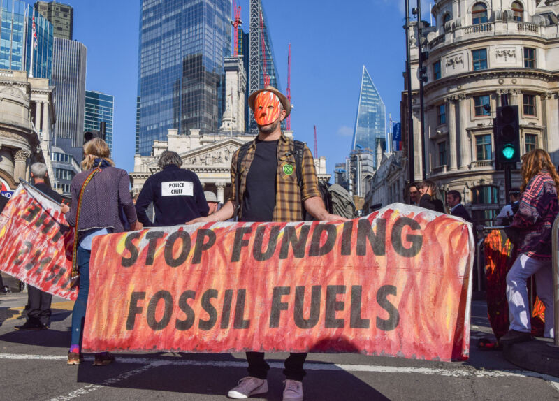 A protester wearing a mask holds an anti-fossil fuels banner