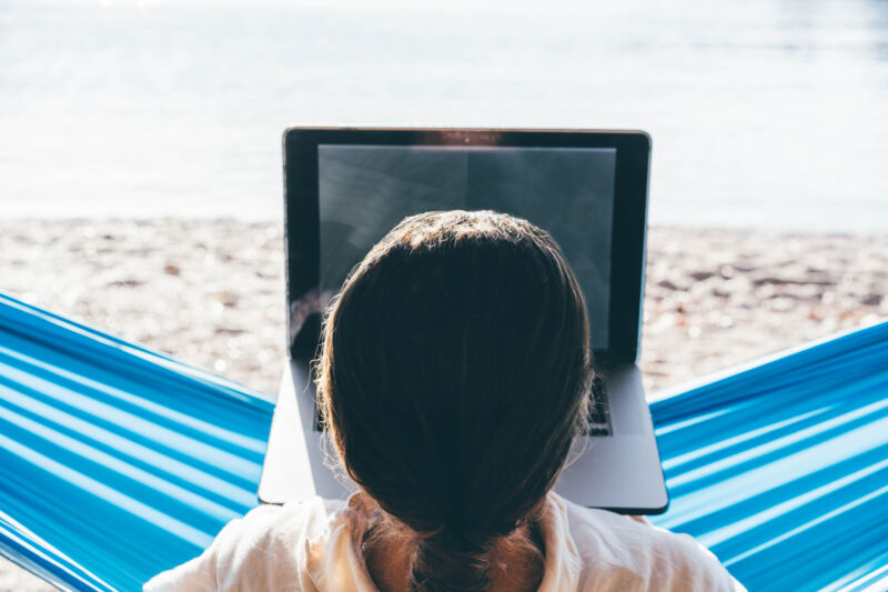 Woman using laptop in hammock on beach.