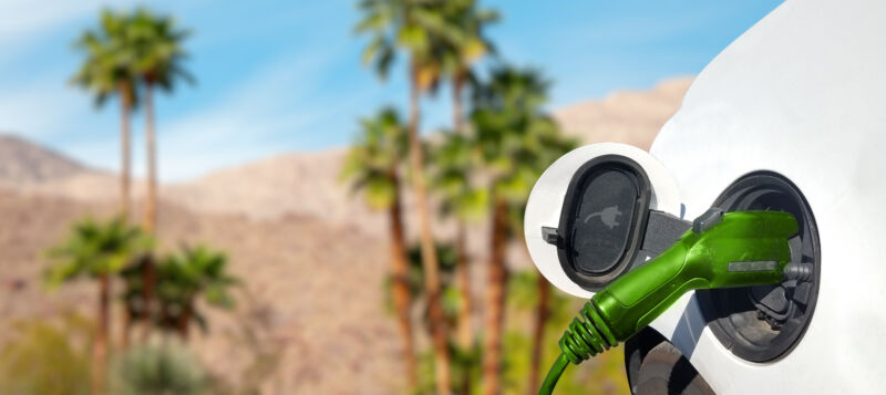 Close up view of Electric Car charging in the desert with palm trees and hills in the background.