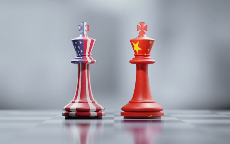 Two king chess pieces with American and Chinese flags on black and white chessboard.