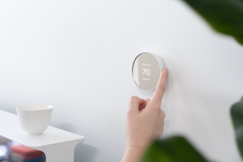Nest thermostat on a wall, being turned by a hand.