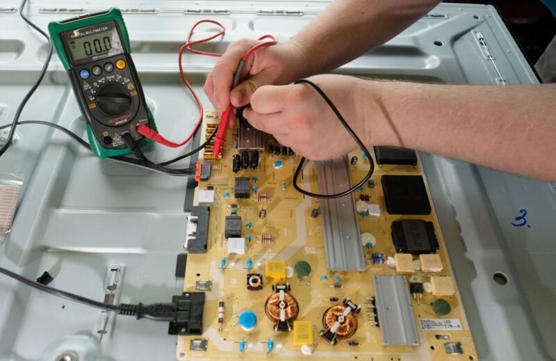 Hands on a circuit board, using multimeter probes to find errors