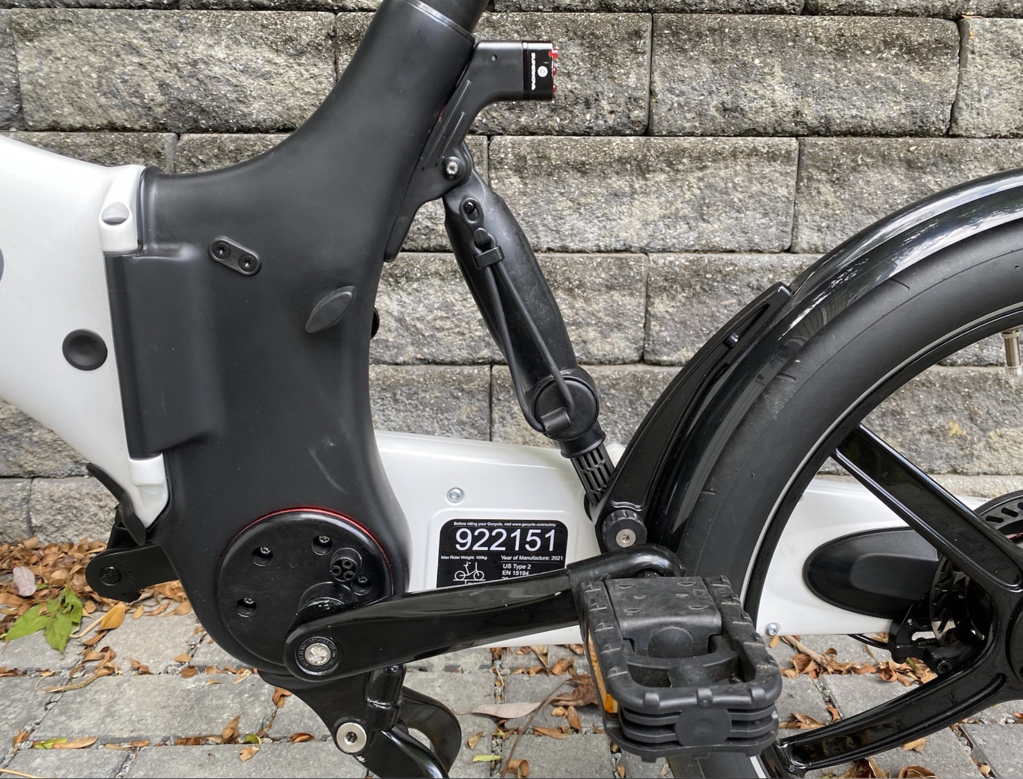 A close-up of the rear suspension. Note the elastic strap stowed on it—when the bike is folded, this clips onto a hook on the handlebars to keep it folded. Also note the black plastic handle to the left, which can be turned to release the seat post for storage.