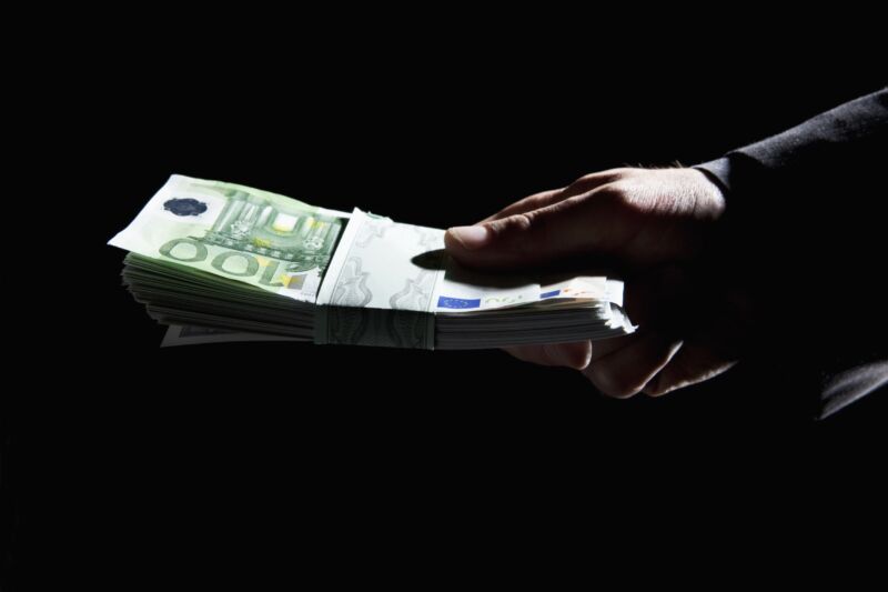 A man's holding holding a stack of 100-euro bills.