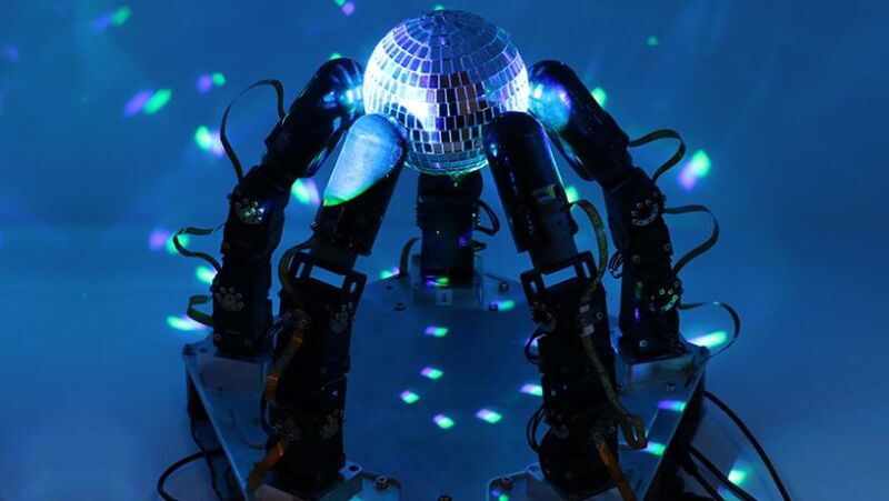 Image of robotic fingers gripping a mirrored disco ball with light reflected off it.